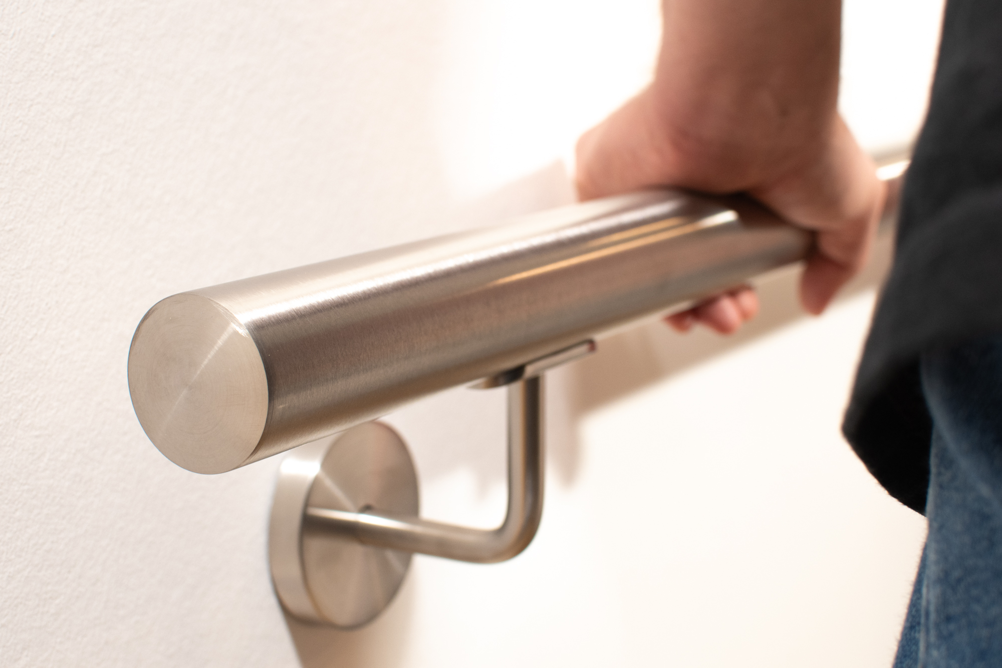 Pasamanos de acero inoxidable redondo en pared blanca con soporte de acero inoxidable, una mano lo agarra, testa plana