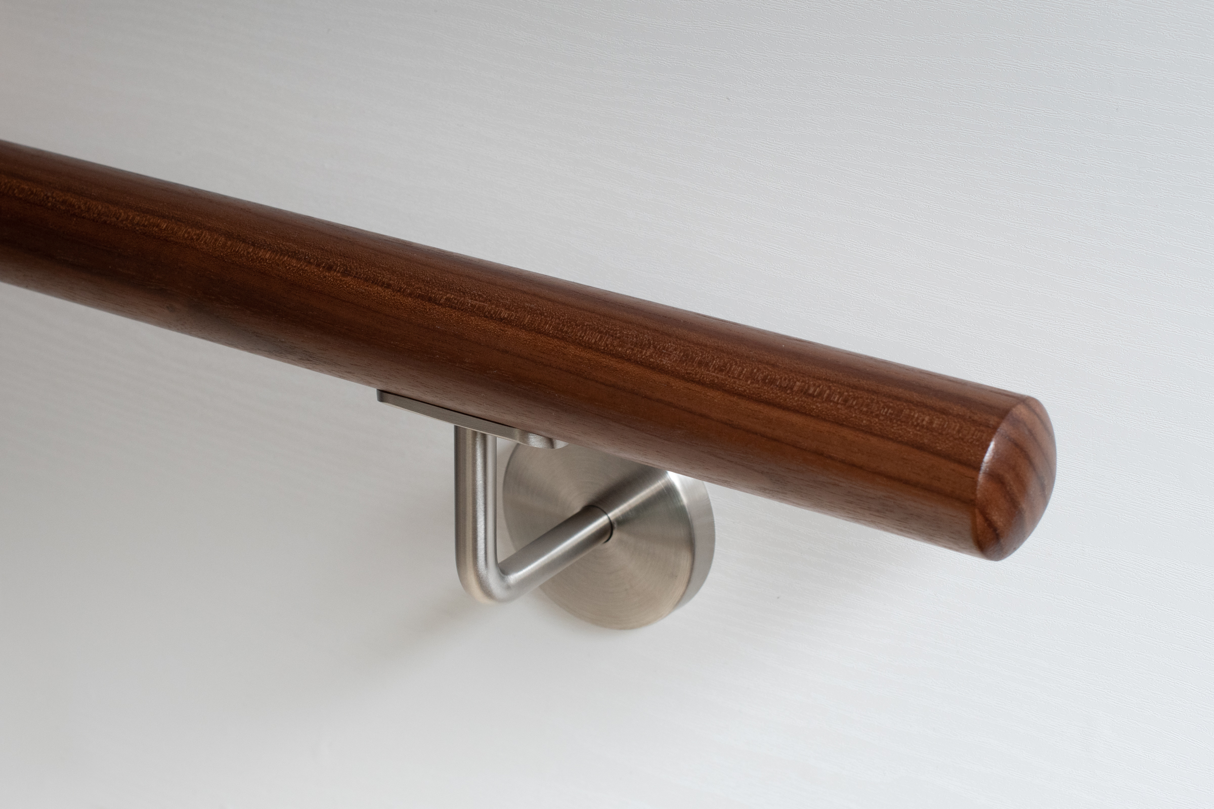 Pasamanos redondo de nogal con soporte de acero inoxidable en pared blanca, madera marrón oscuro, detalle del extremo