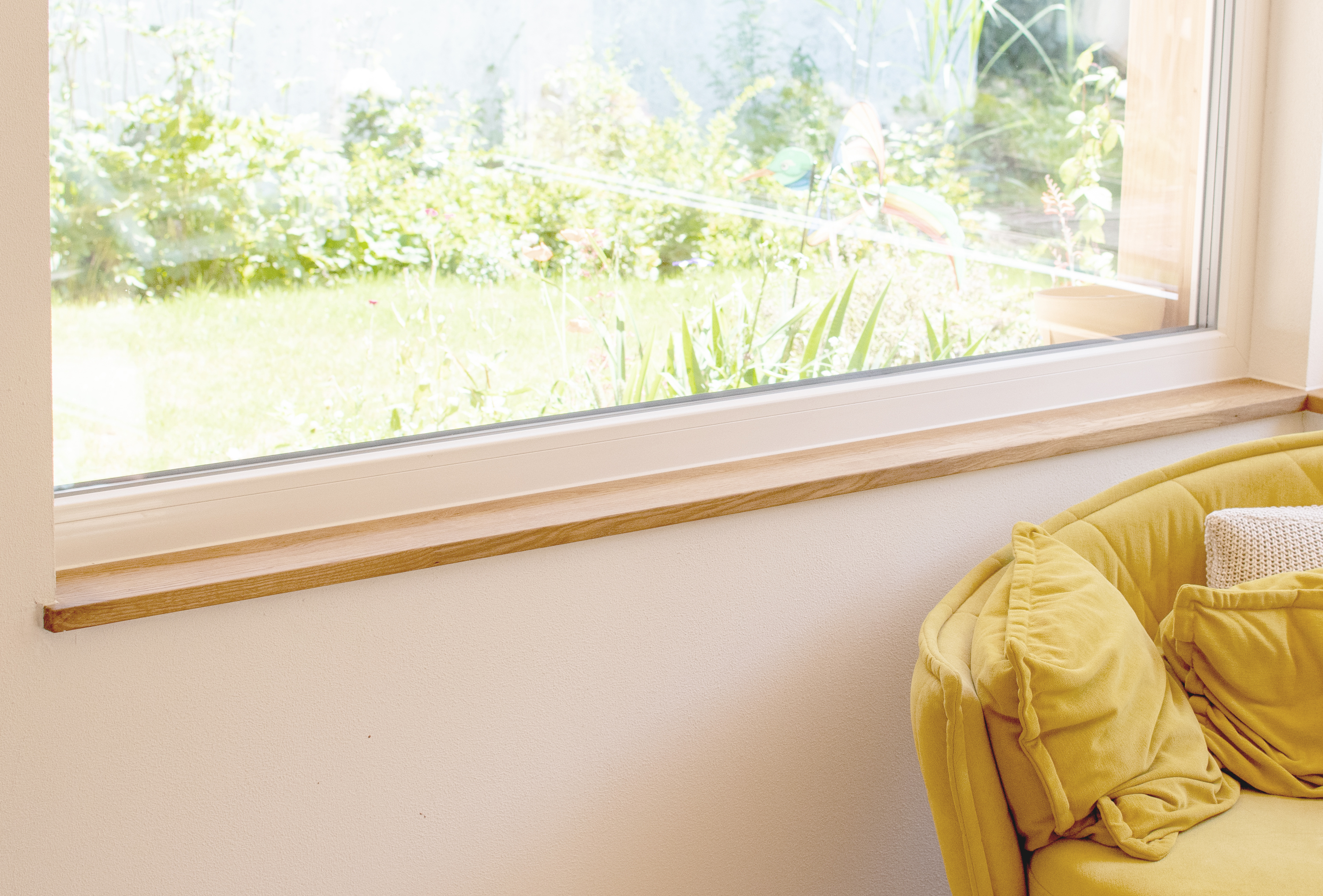 Alféizar de madera estrecho y claro bajo ventana ancha con vista al jardín, sofá amarillo con cojines en el salón