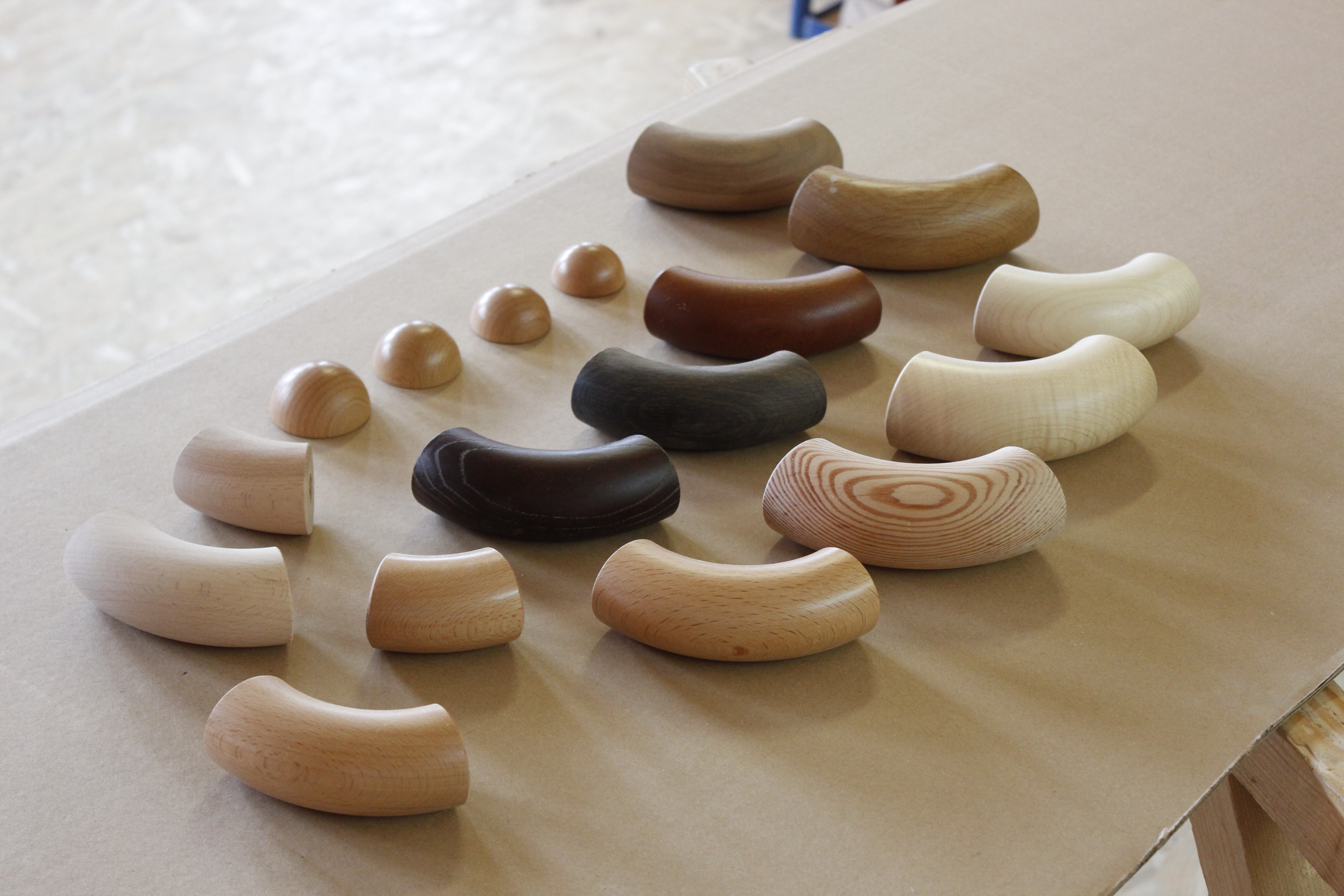 Accesorios de madera para pasamanos: codos y remates semiesféricos de distintas maderas sobre papel en el taller