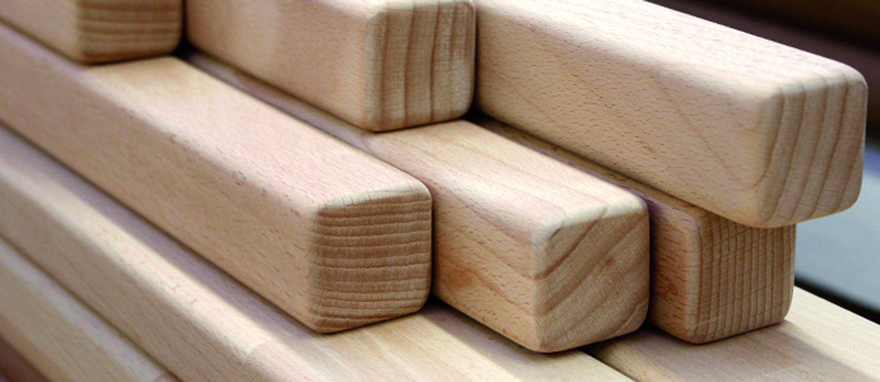 Pasamanos cuadrados de madera apilados, madera clara con cantos biselados y testas visibles, primer plano