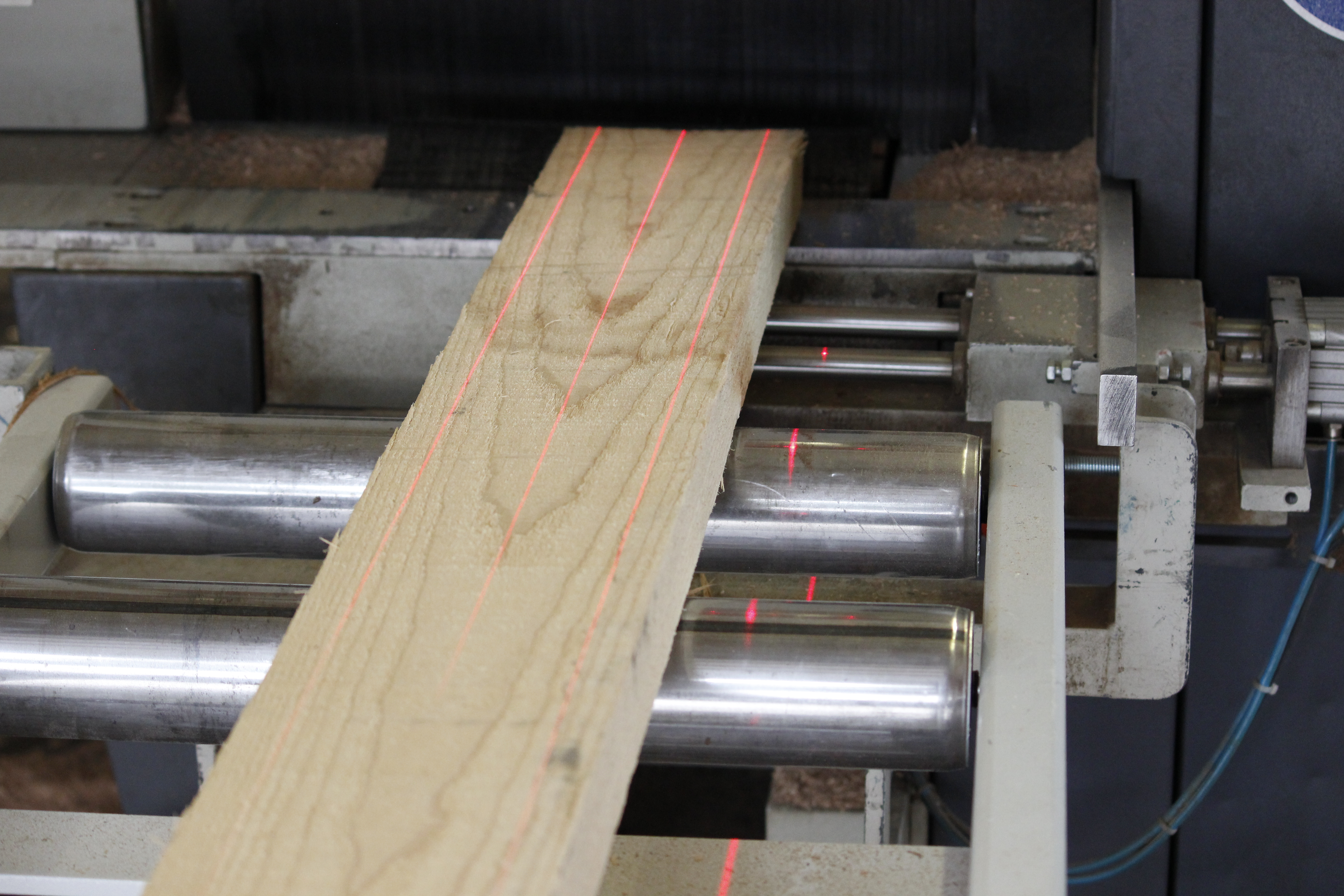 Tablón de madera sobre rodillos con líneas láser rojas durante el corte a medida en la fabricación de alféizares