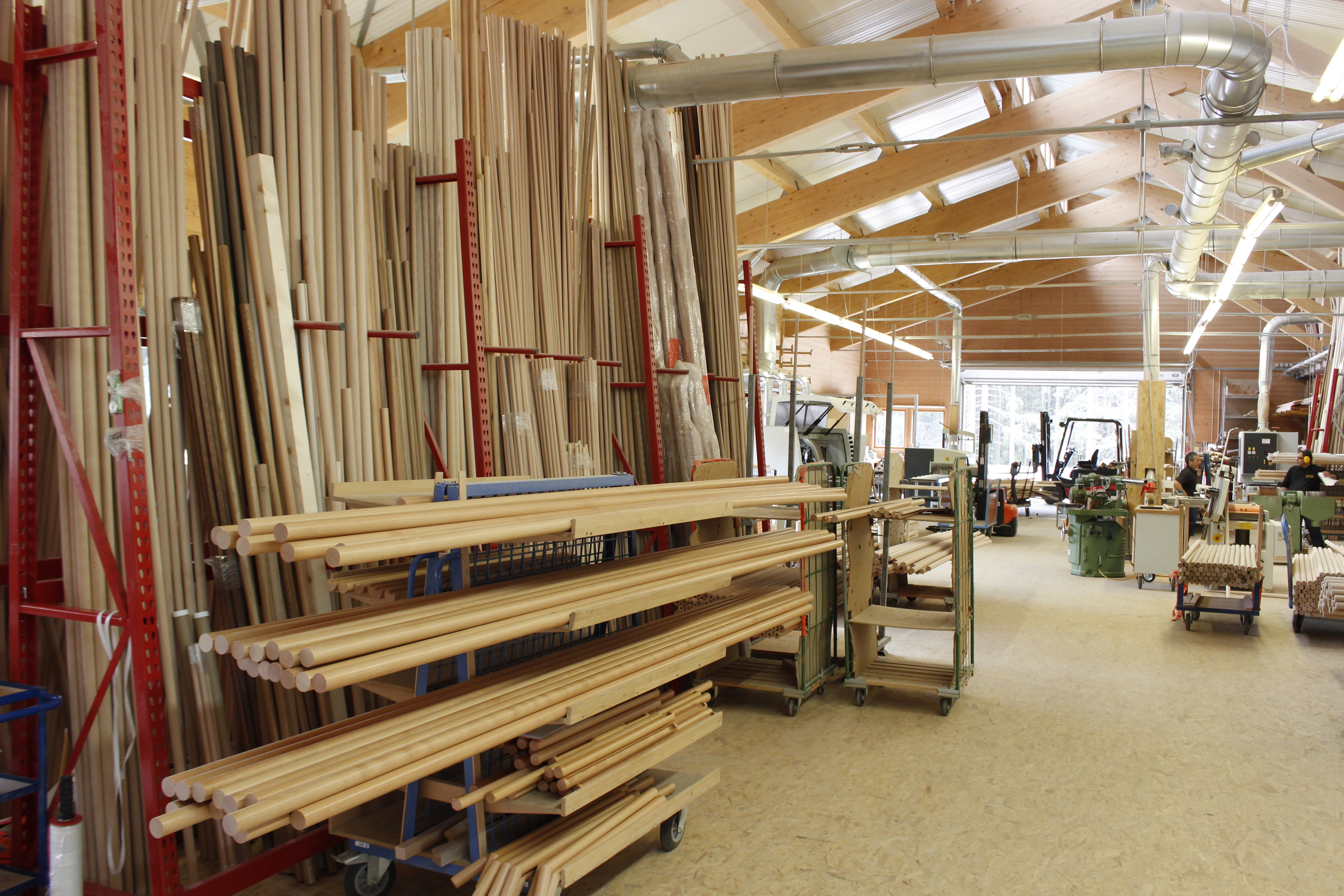 Pasamanos de madera y barras redondas en el almacén de la tornería, largas varillas en estanterías cantilever rojas