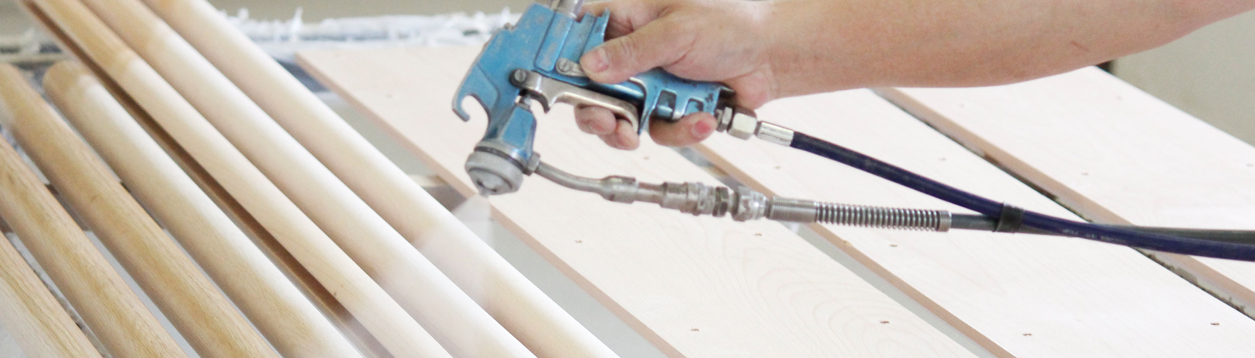 Fabricación de pasamanos: pasamanos de madera lacados con pistola, mano con pistola de pintura sobre varillas claras