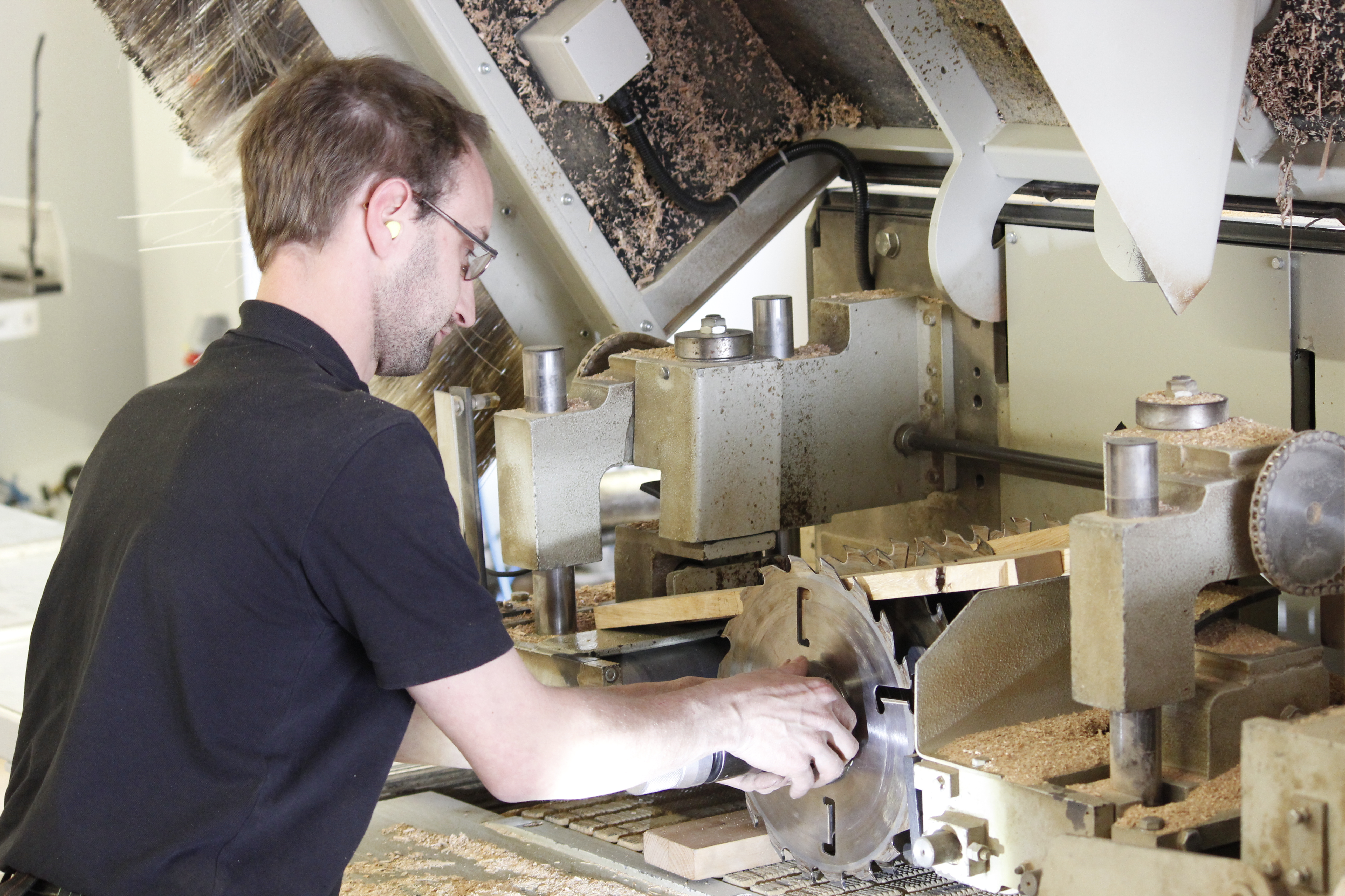 Carpintero en una cepilladora del taller trabajando madera maciza, con virutas sobre la máquina