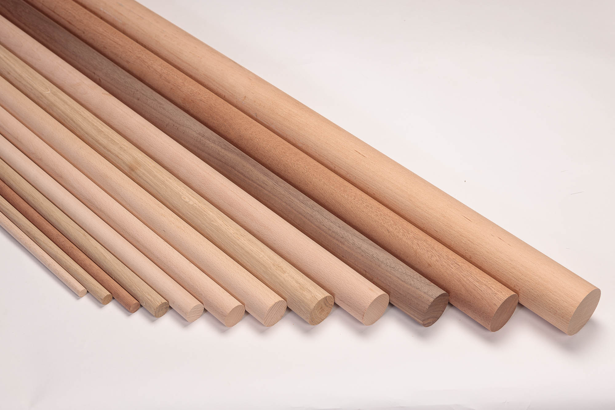 Barras redondas de madera de distintos diámetros y maderas escalonadas una junto a otra, de maderas claras a rojizas
