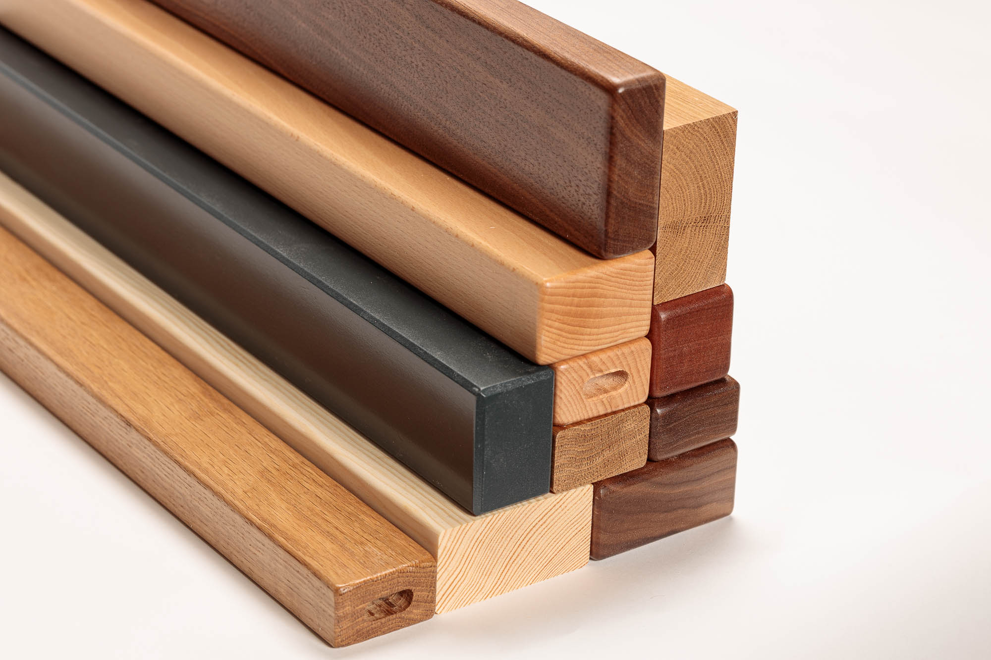 Pasamanos de madera rectangulares apilados en distintas maderas y colores, perfiles claros, oscuros y lacados en negro