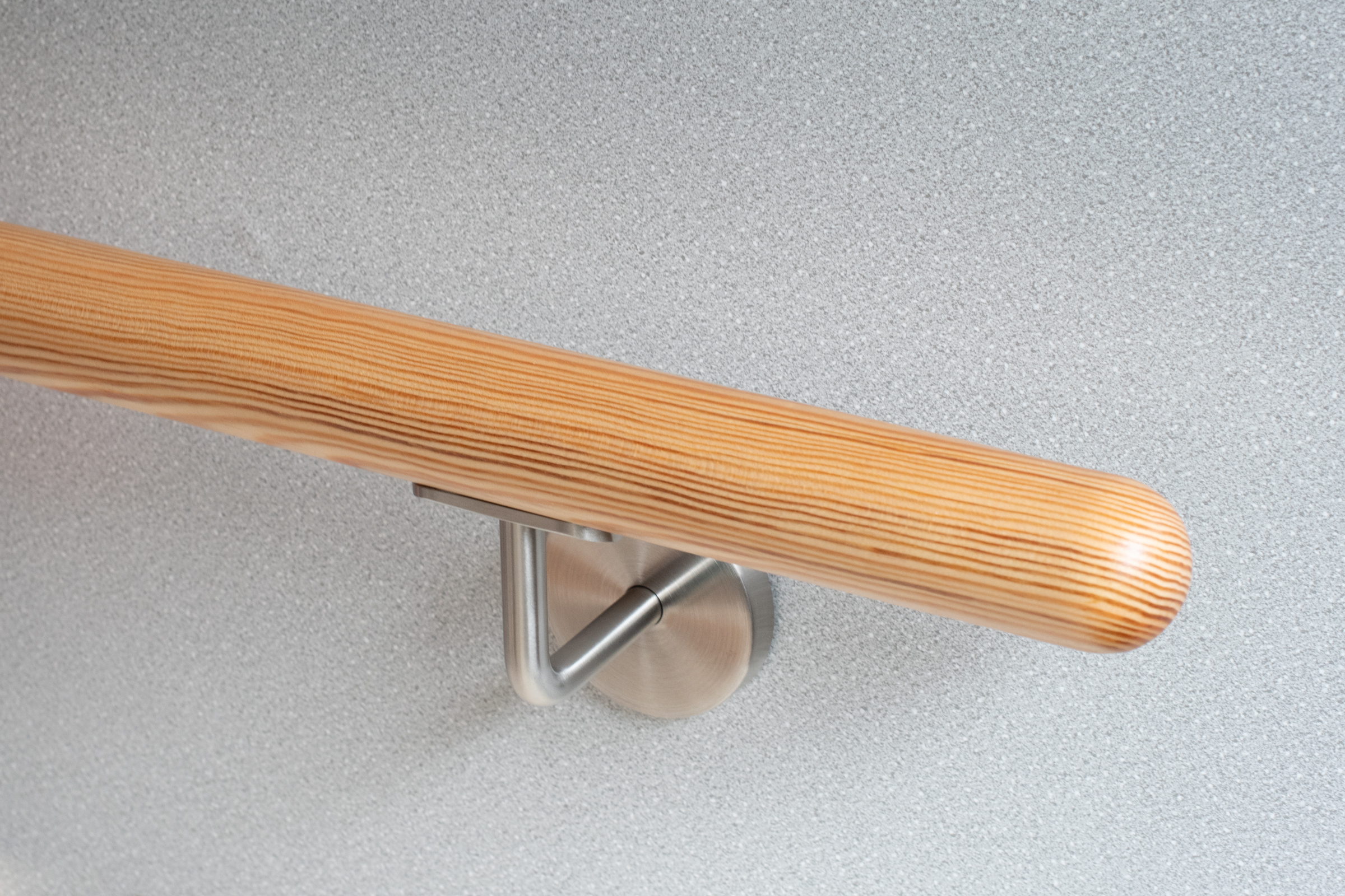 Pasamanos redondo de pino con soporte de acero inoxidable ante pared gris claro, conífera con veteado visible, primer plano