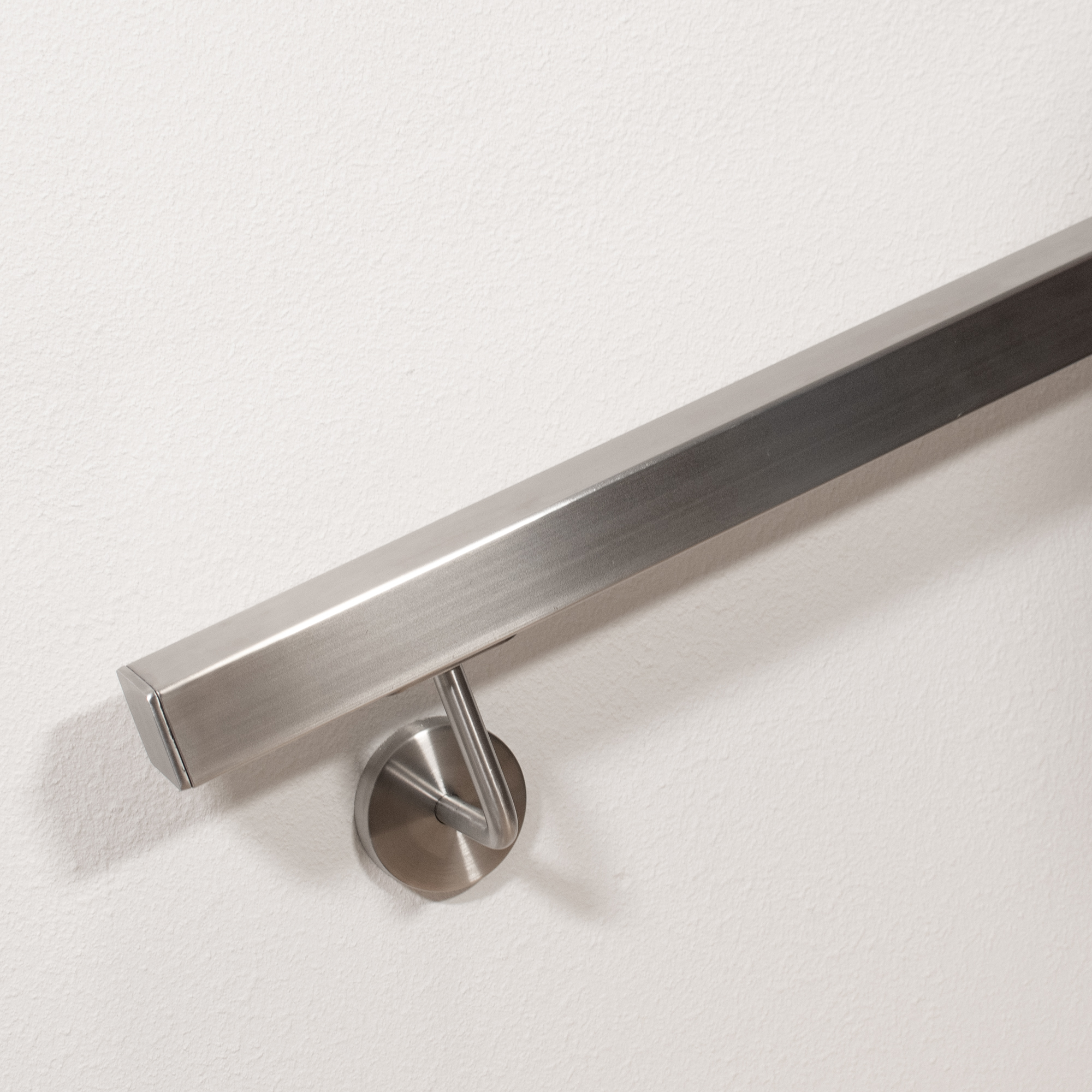 Pasamanos cuadrado de acero inoxidable con remate plano y soporte curvado, detalle del extremo en una pared blanca