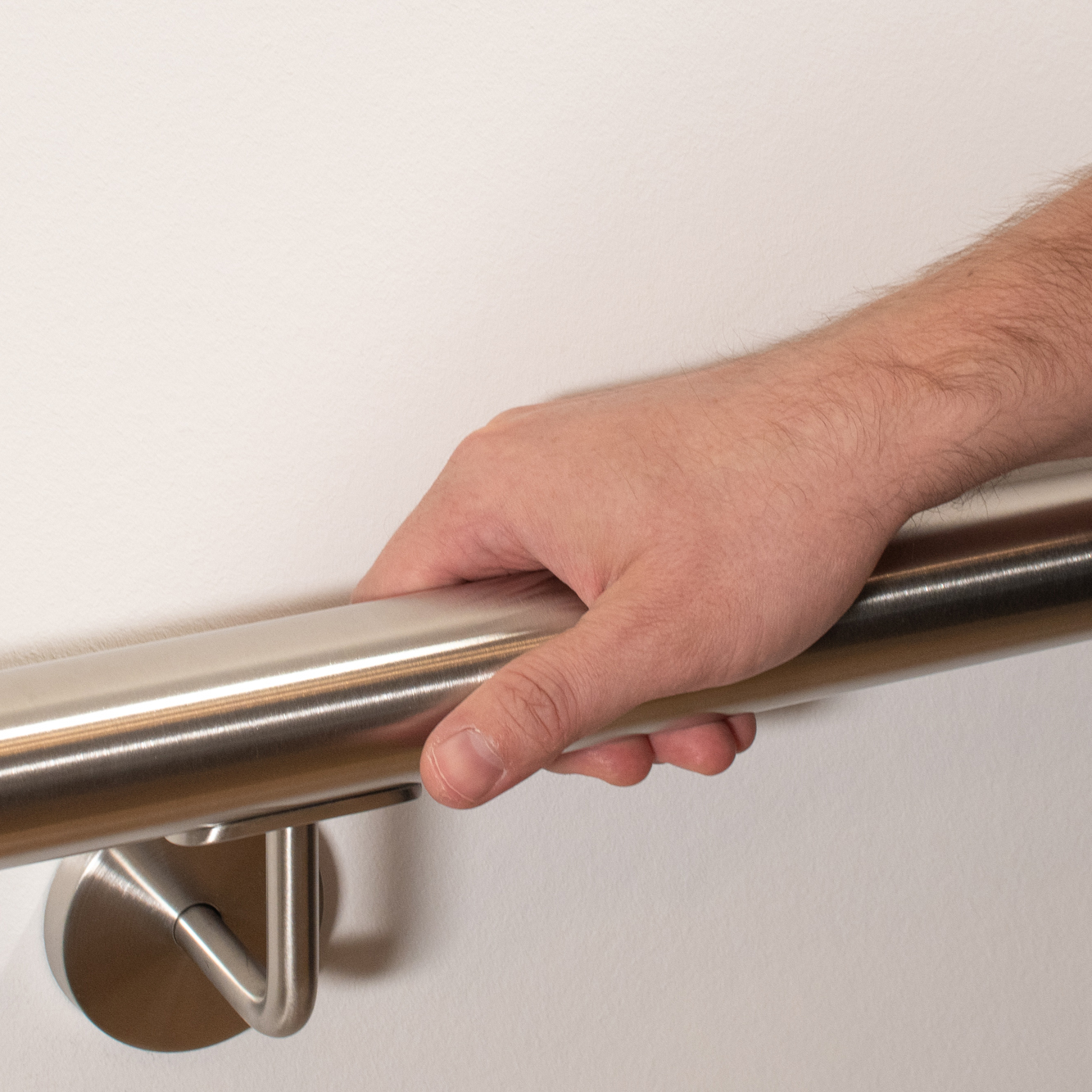 Pasamanos de acero inoxidable redondo en pared blanca con soporte de acero inoxidable, una mano lo rodea, primer plano