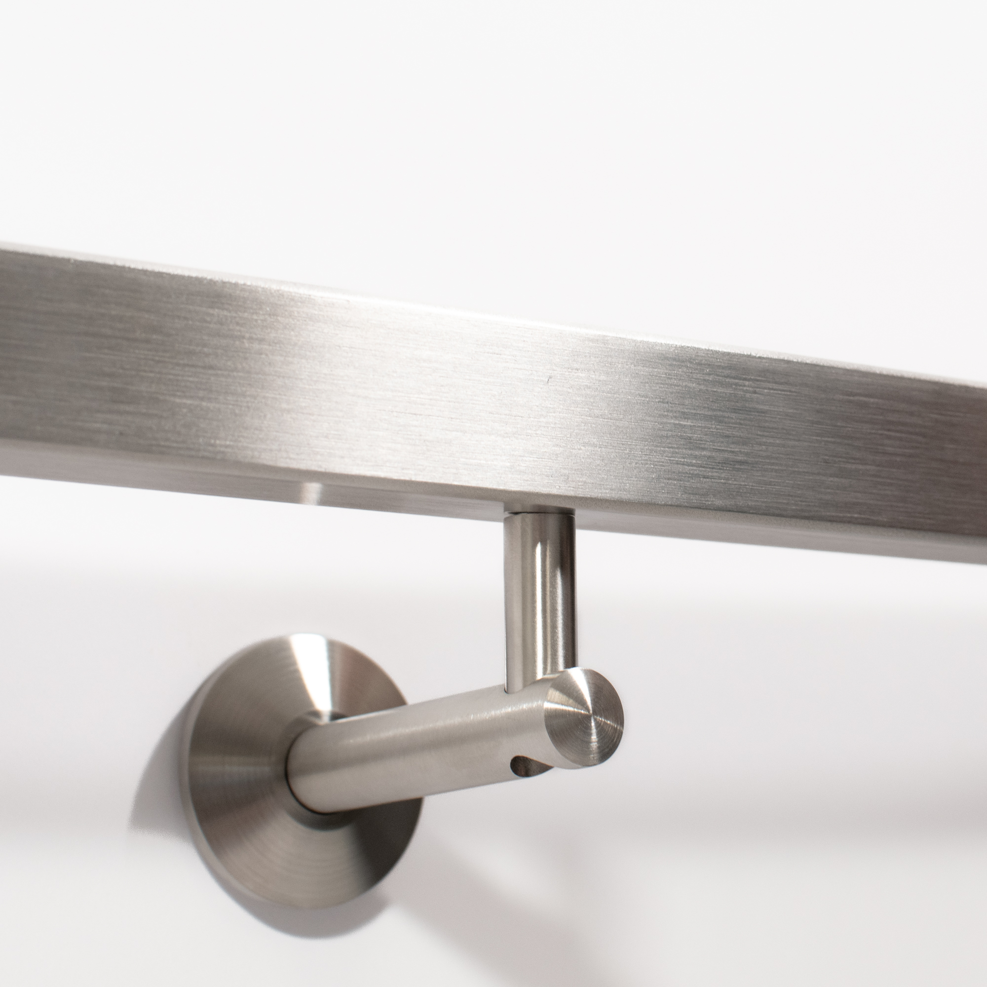 Pasamanos cuadrado de acero inoxidable con soporte de pared y roseta, primer plano desde abajo en una pared blanca