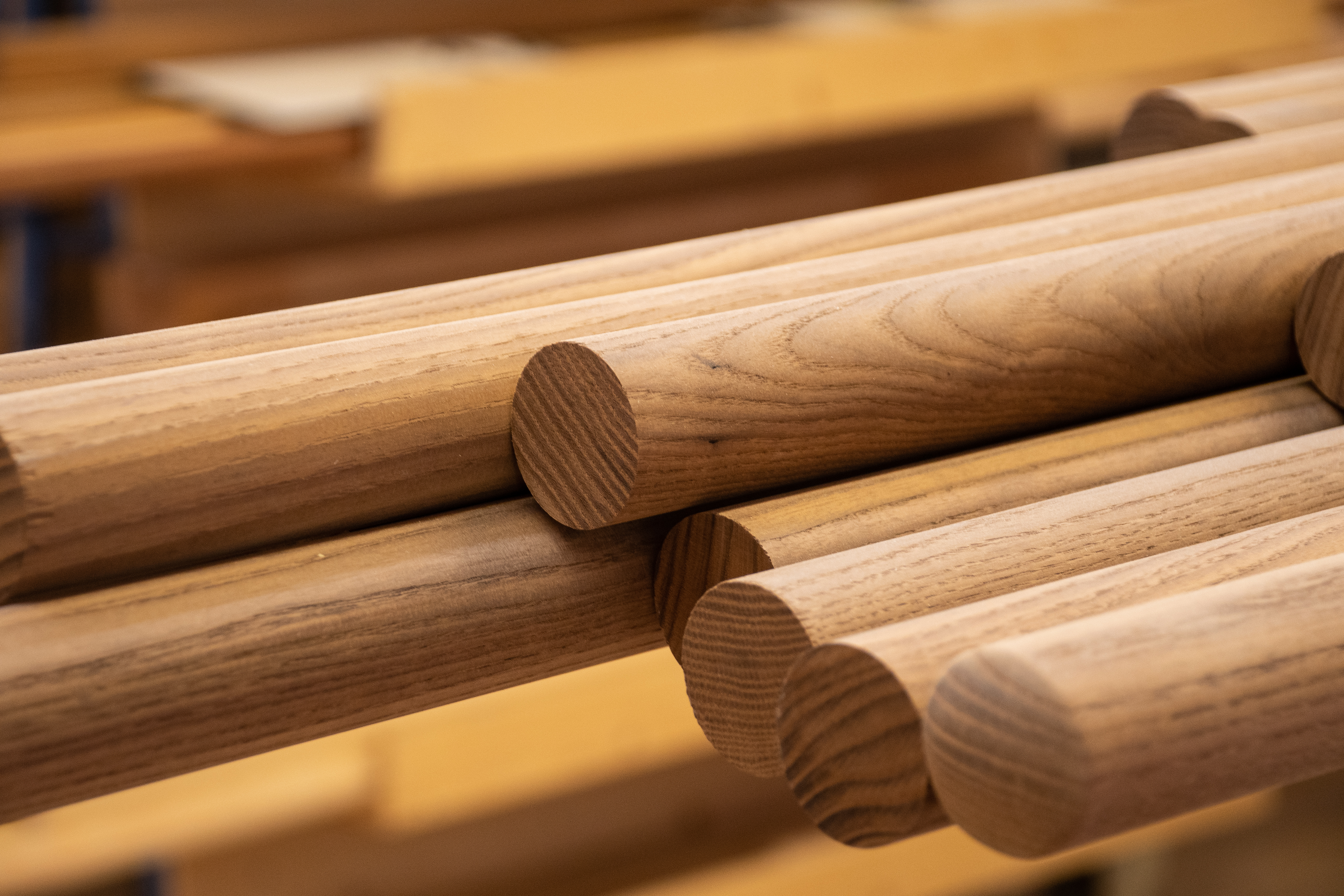Pasamanos redondos de madera apilados en la estantería del taller, barras con testas y veteado visibles, primer plano