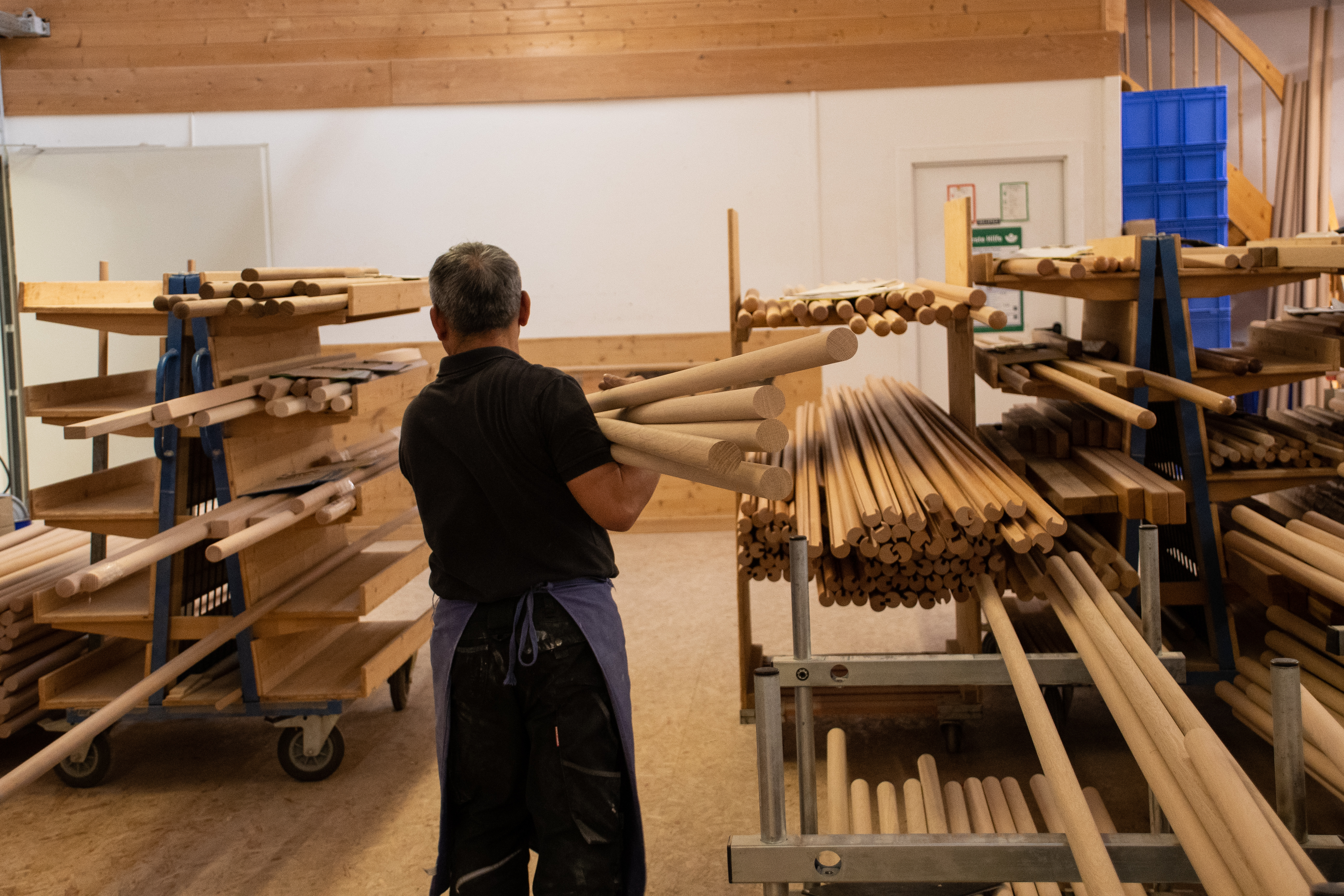 Barras redondas de madera en la estantería del taller, un empleado clasifica barras en la tornería, muchos diámetros
