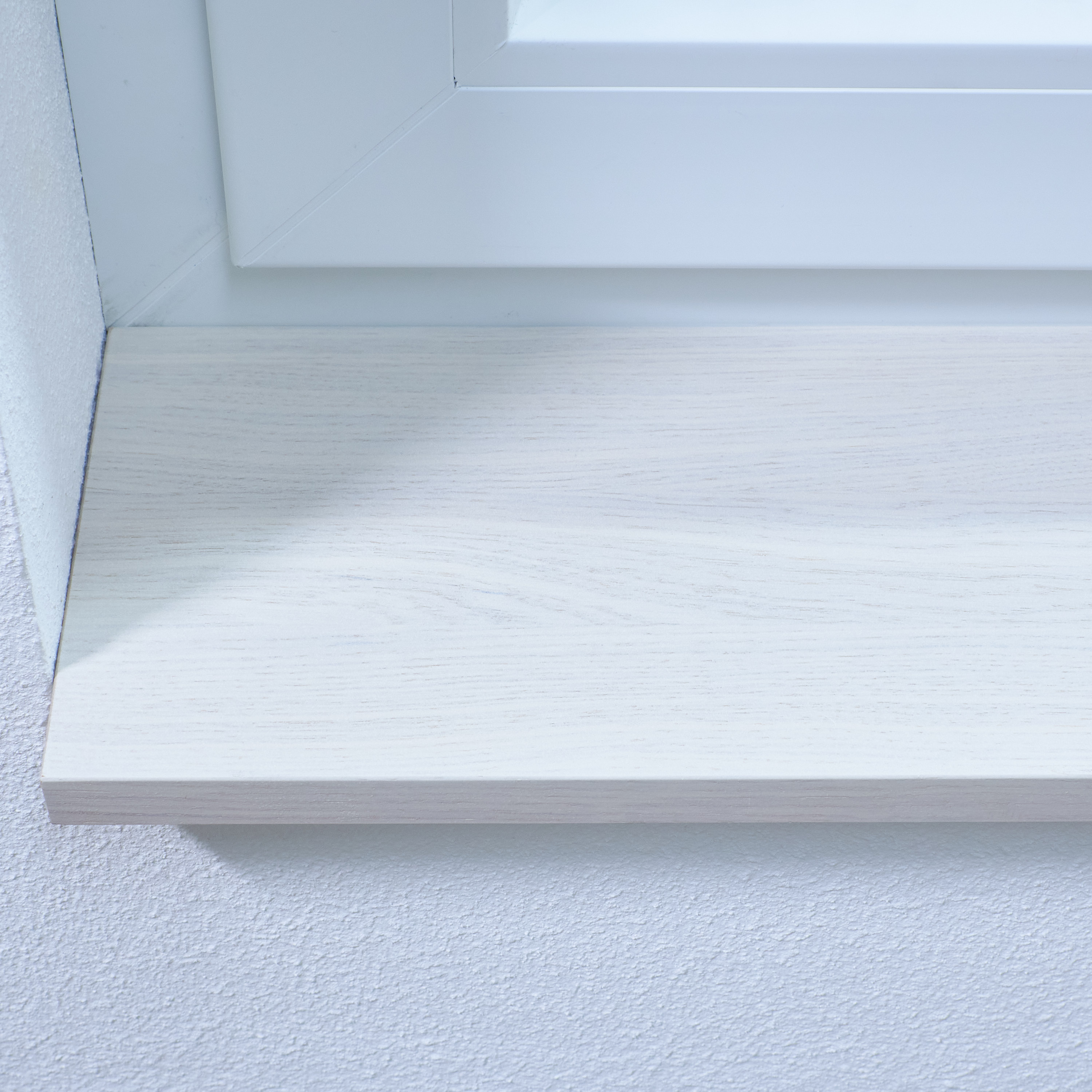 Alféizar teñido de blanco con veteado visible, primer plano del canto frontal bajo el marco blanco de la ventana