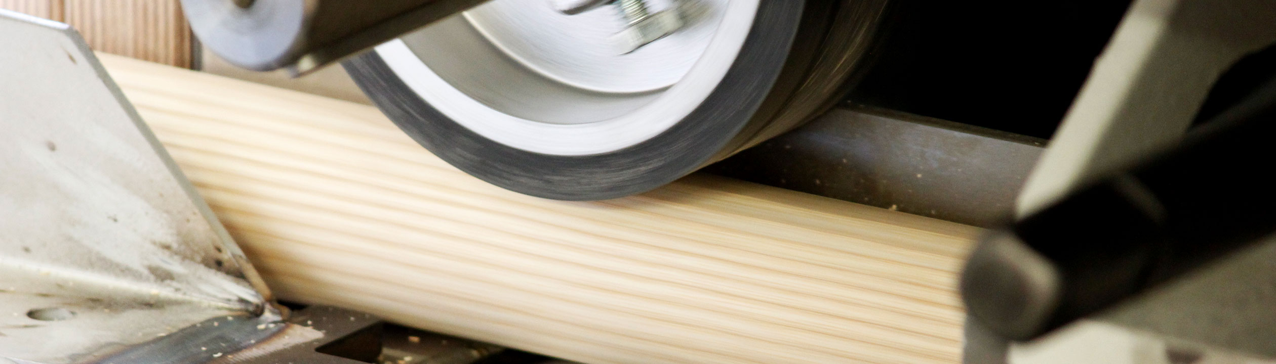 Fabricación de pasamanos: barra redonda de madera en la lijadora, primer plano del rodillo de lijado, formato banner