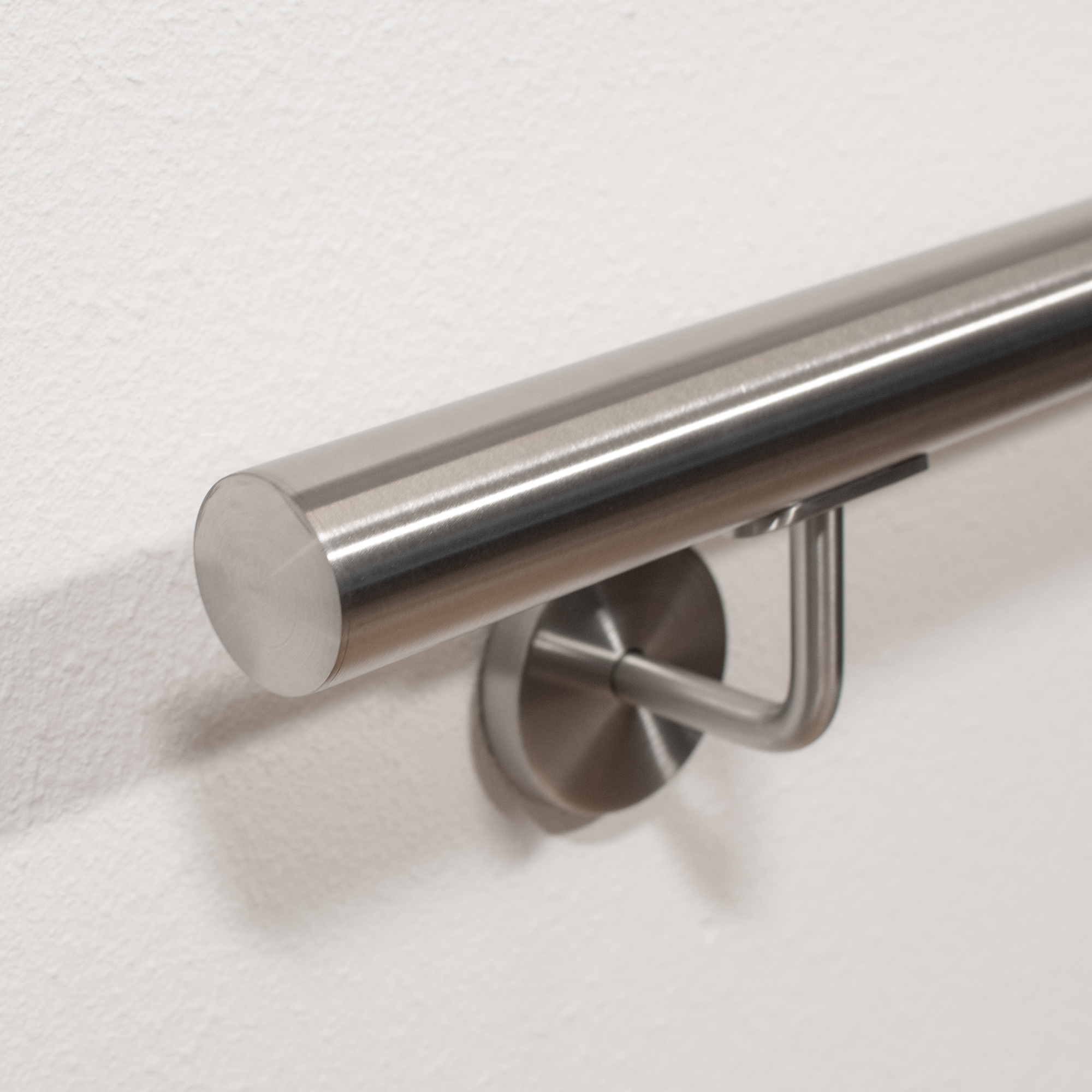 Pasamanos de acero inoxidable redondo con soporte de acero inoxidable y remate plano en pared blanca, detalle desde abajo