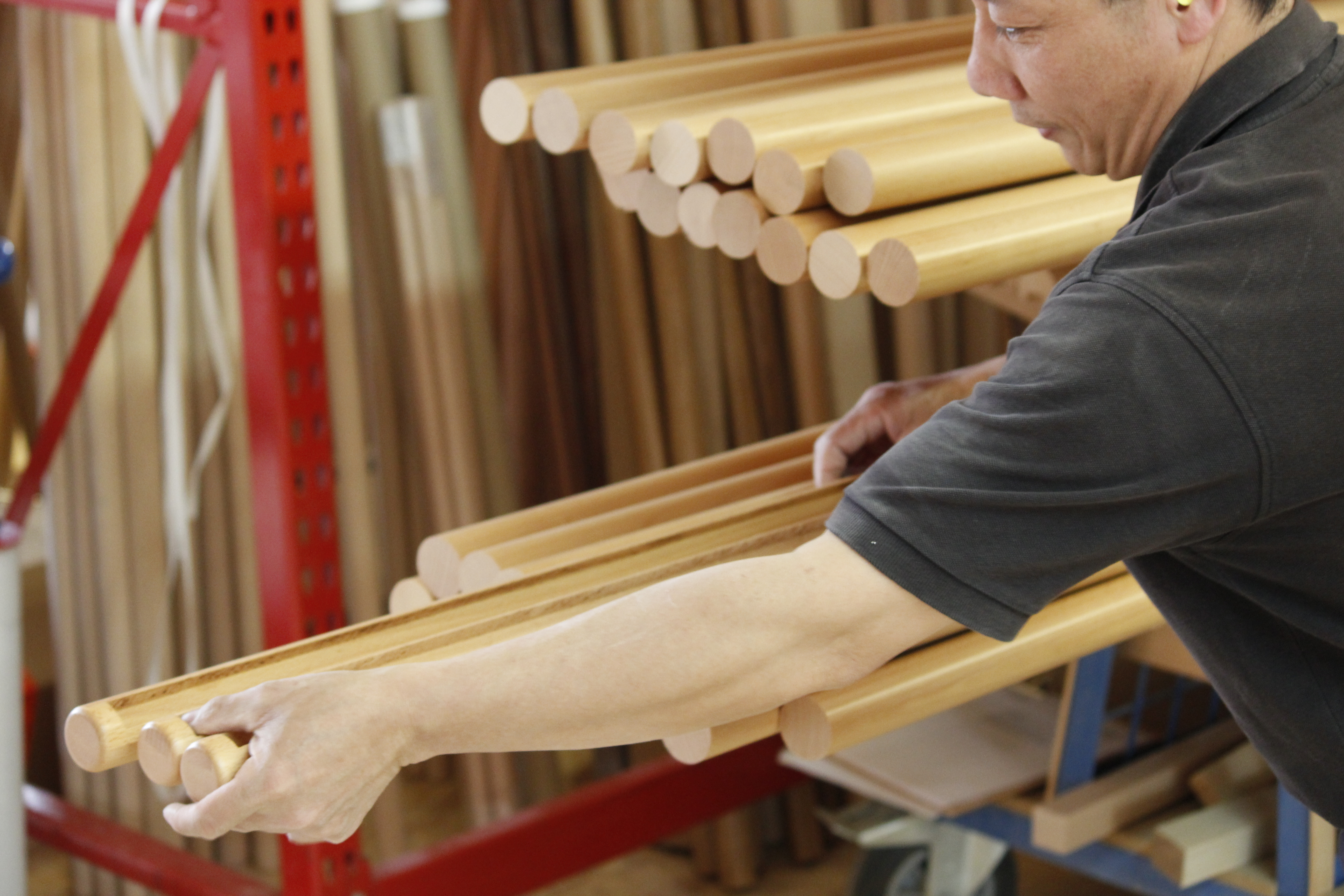 Control de calidad de pasamanos redondos de madera: empleado revisa las varillas a mano junto a la estantería del taller