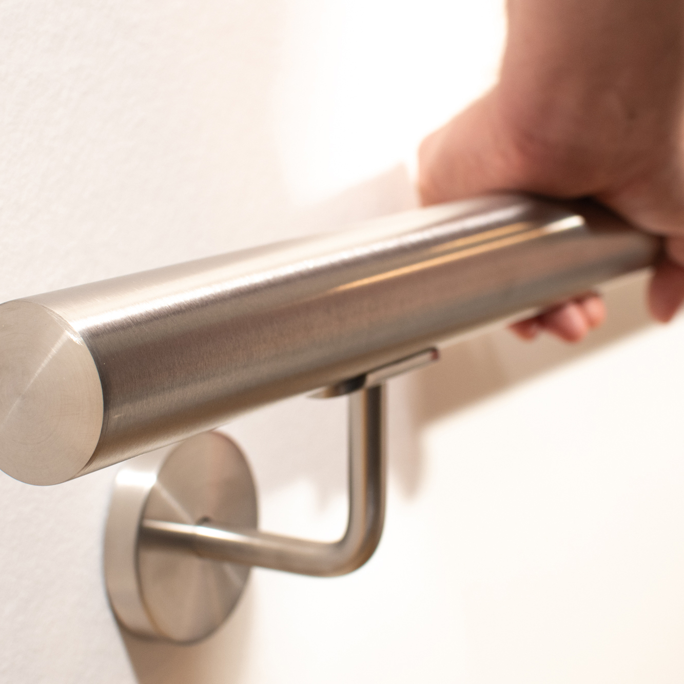 Pasamanos redondo de acero inoxidable en pared blanca con soporte de acero inoxidable, una mano agarra el tubo cepillado