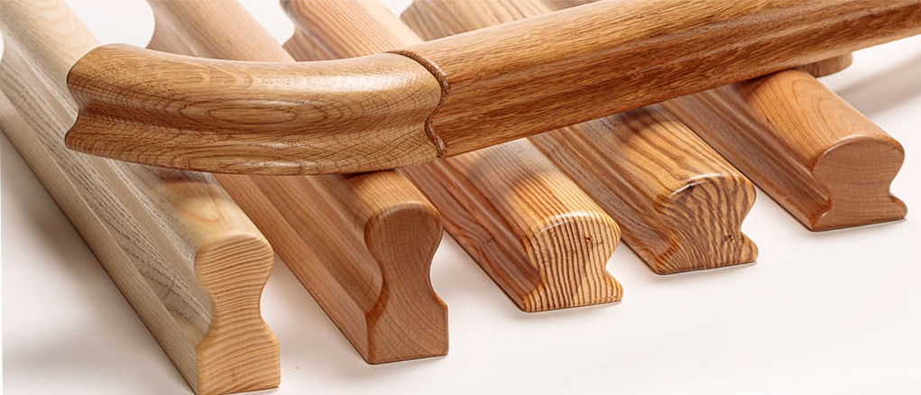 Pasamanos Omega de madera de distintas especies, apilados, perfil Omega con ranura y testas visibles, primer plano
