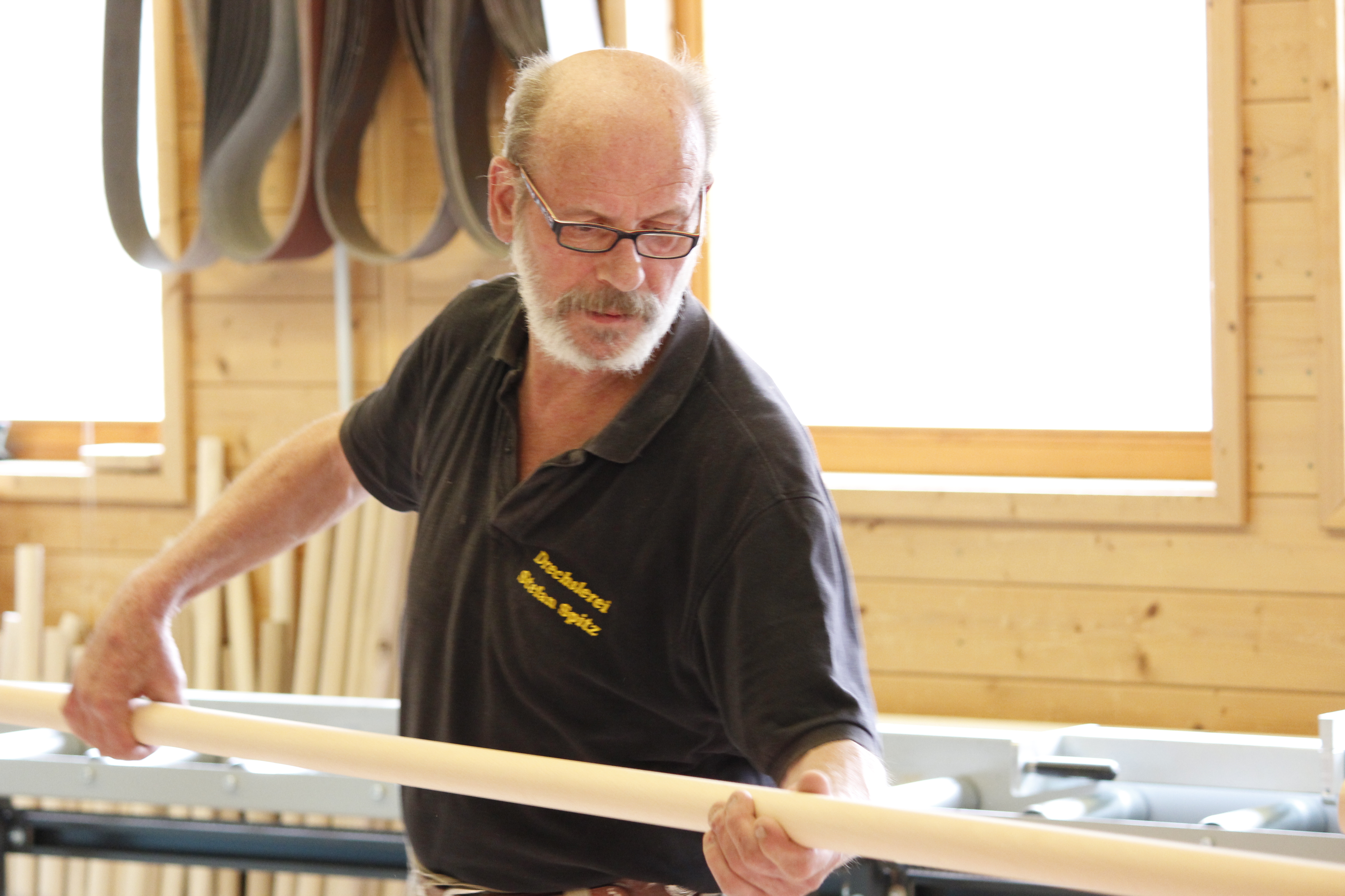 Fabricación de pasamanos: un empleado revisa un pasamanos redondo de madera en el taller, pared de madera y banco al fondo