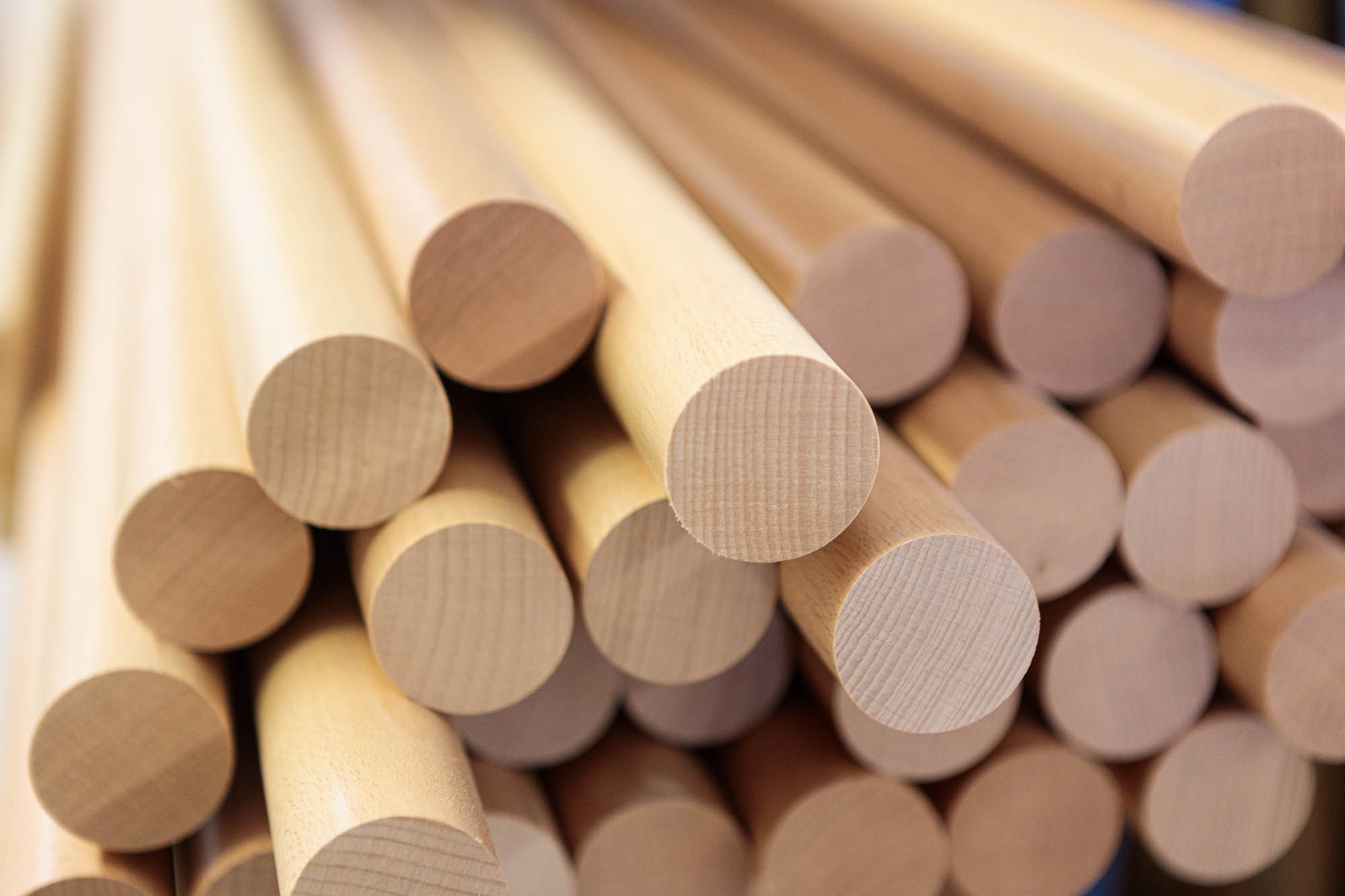 Pasamanos redondos de madera apilados, barras claras con testas visibles en el taller, primer plano