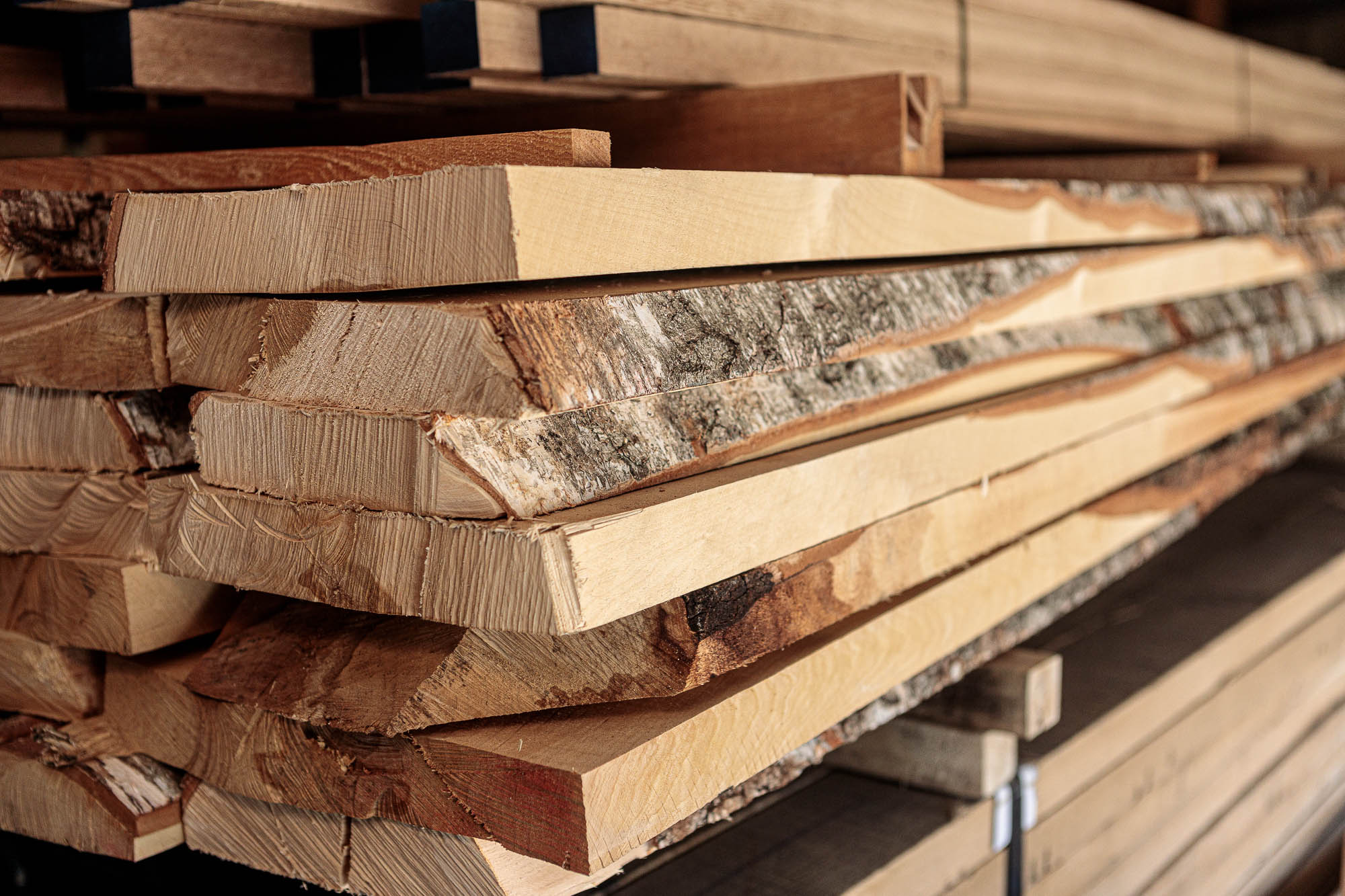 Almacén de madera con tablas sin cantear apiladas, madera clara recién aserrada con corteza en los cantos, primer plano