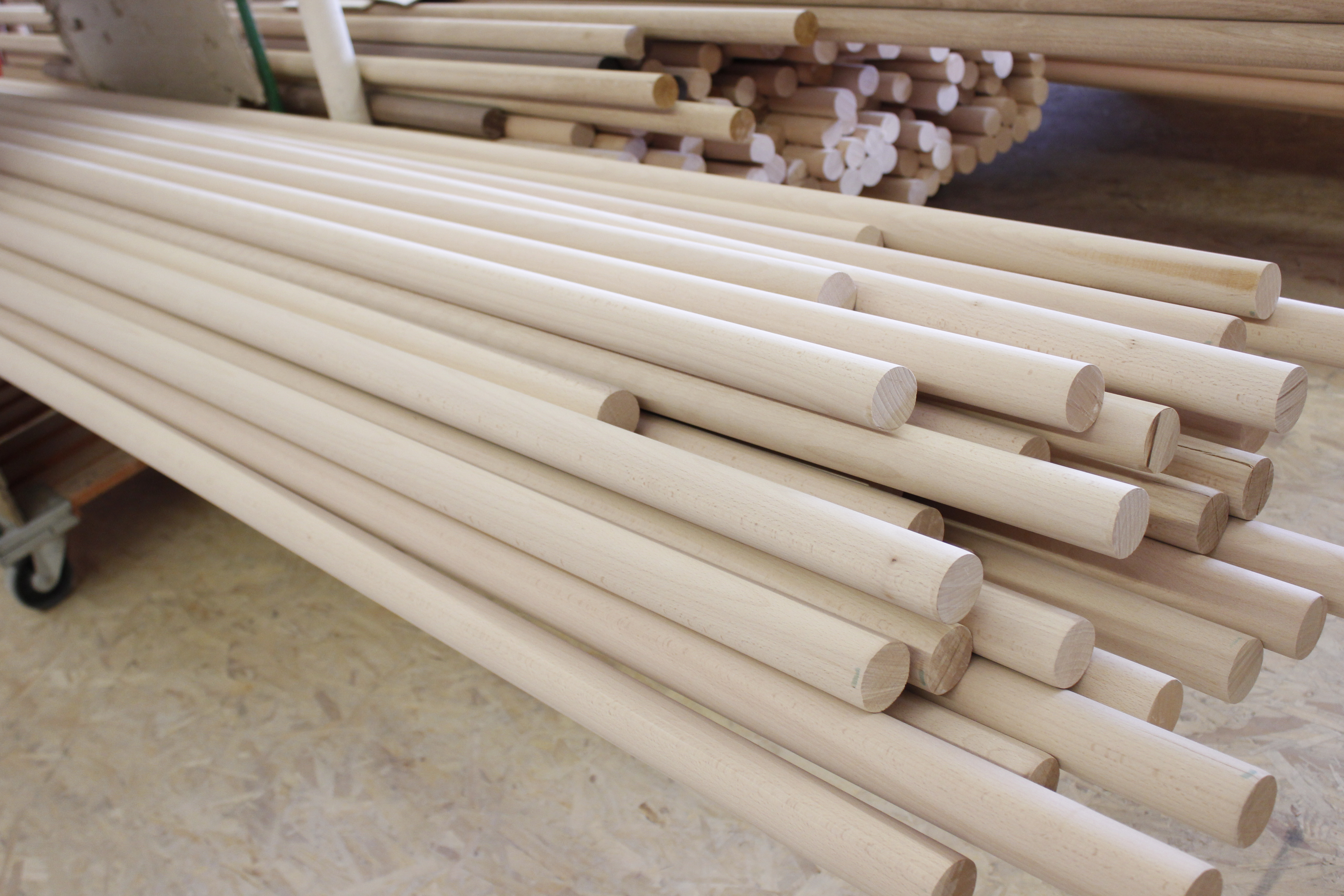 Pasamanos redondos de madera en bruto apilados en un carro en el taller, madera clara sin tratar y sin acabado superficial