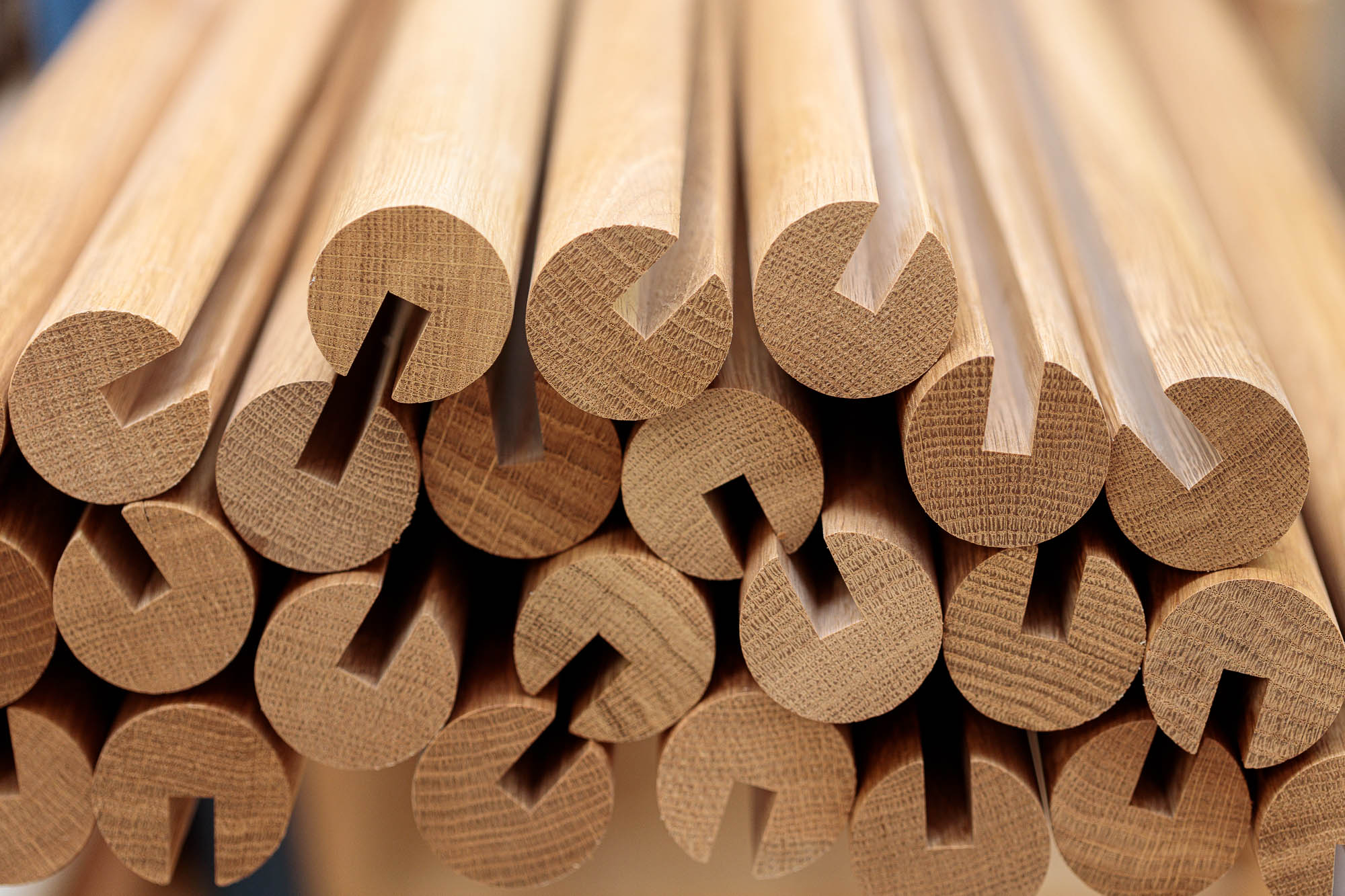 Pasamanos redondos de madera con ranura longitudinal apilados, testas en primer plano, madera dura clara con veteado visible