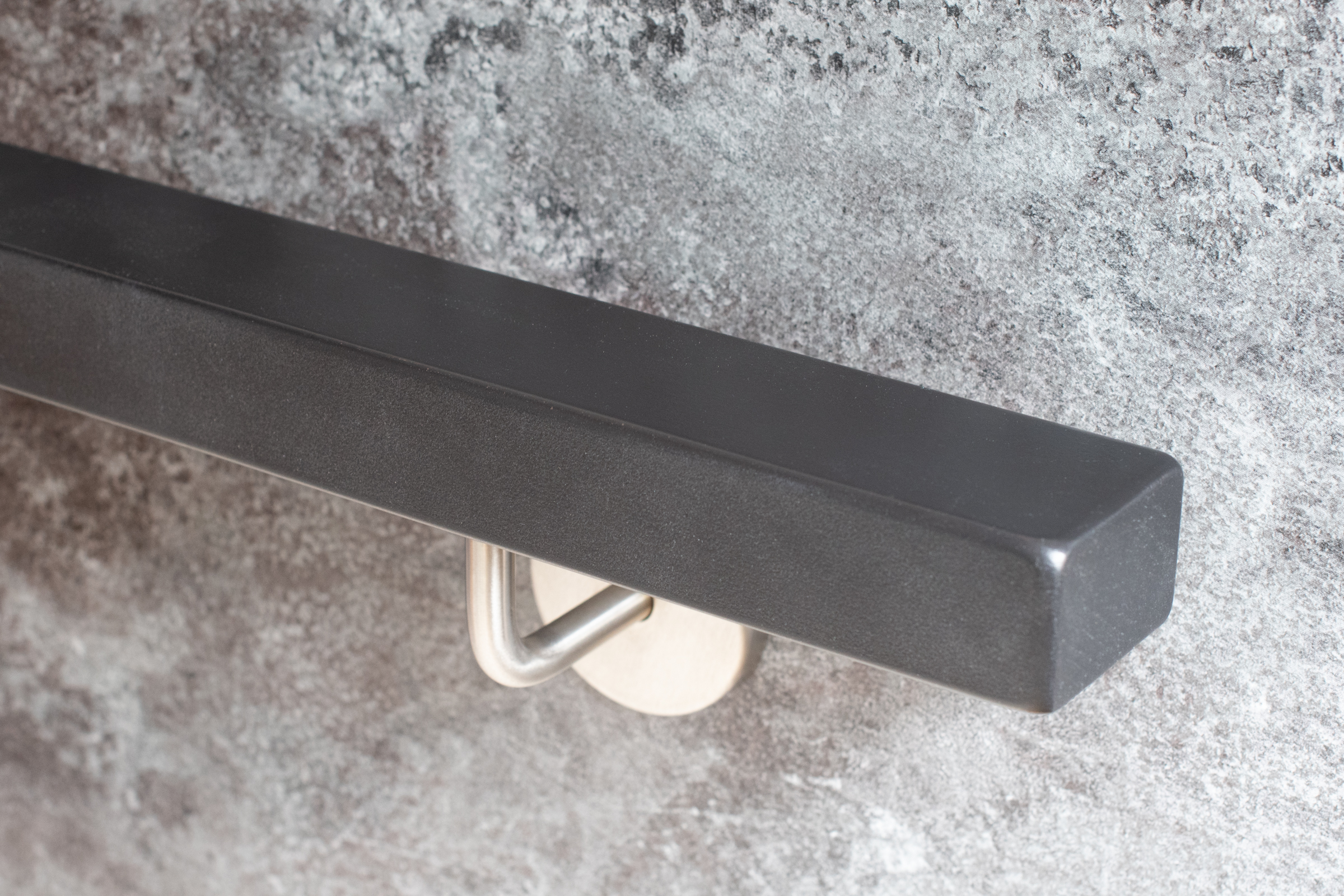 Pasamanos rectangular lacado gris con soporte de acero inoxidable en pared de piedra gris, extremo recto, vista oblicua
