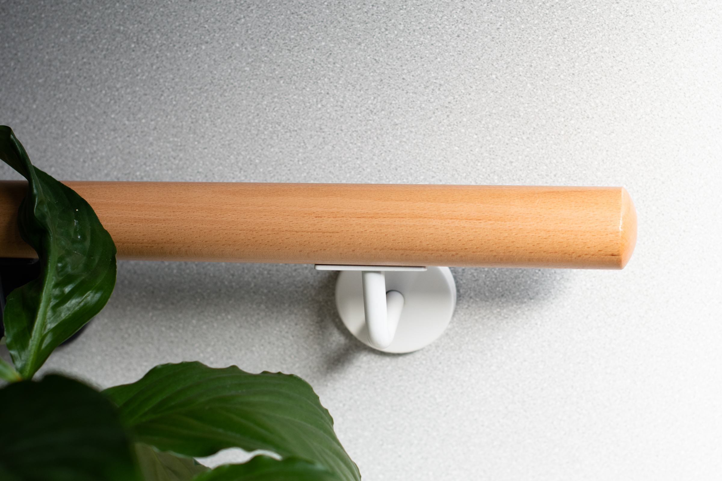 Pasamanos redondo de haya con soporte lacado en blanco en pared gris claro, planta verde de interior en primer plano