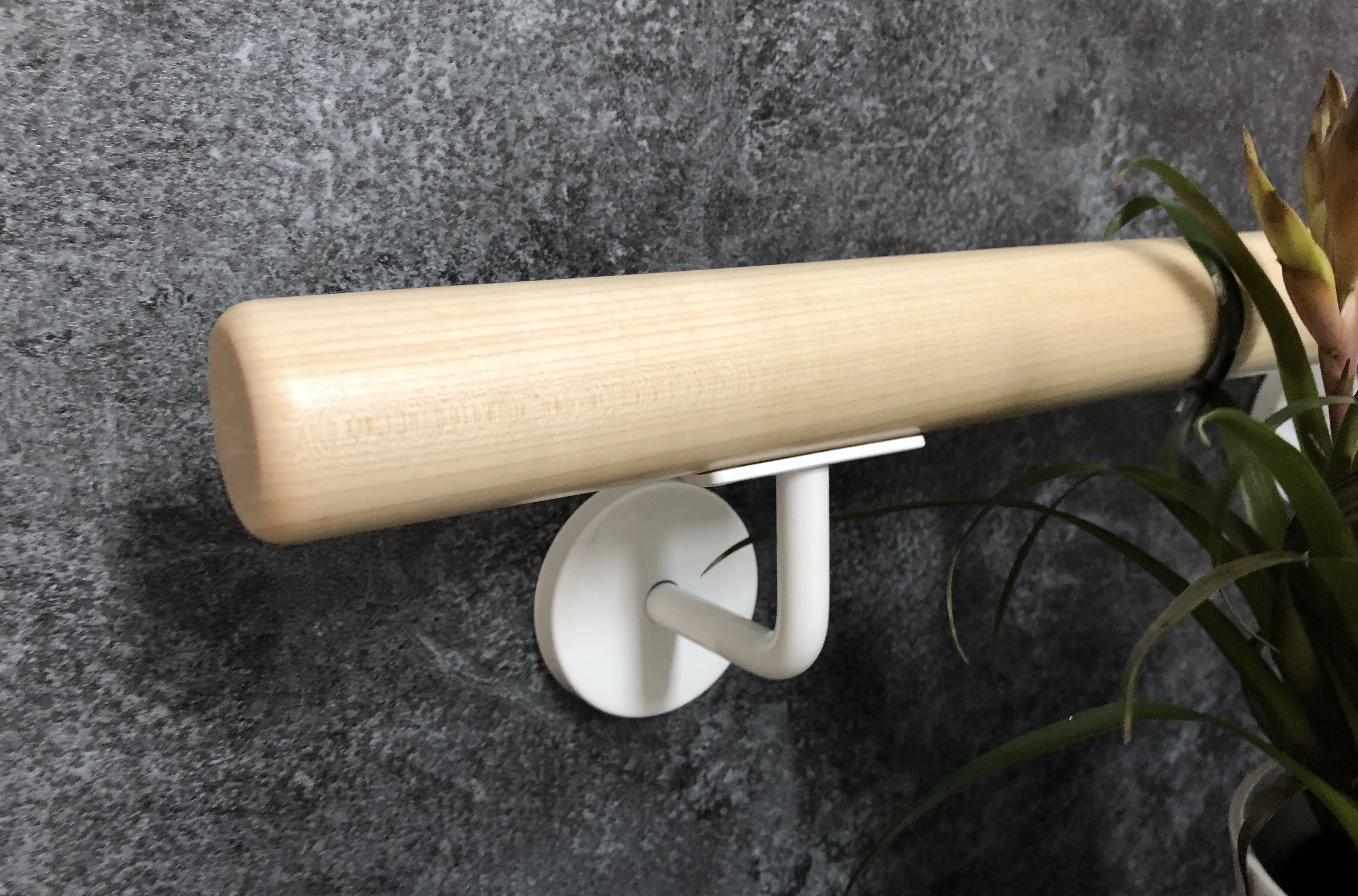 Pasamanos redondo de madera clara con soporte lacado en blanco en pared de piedra gris oscuro, planta verde en el borde