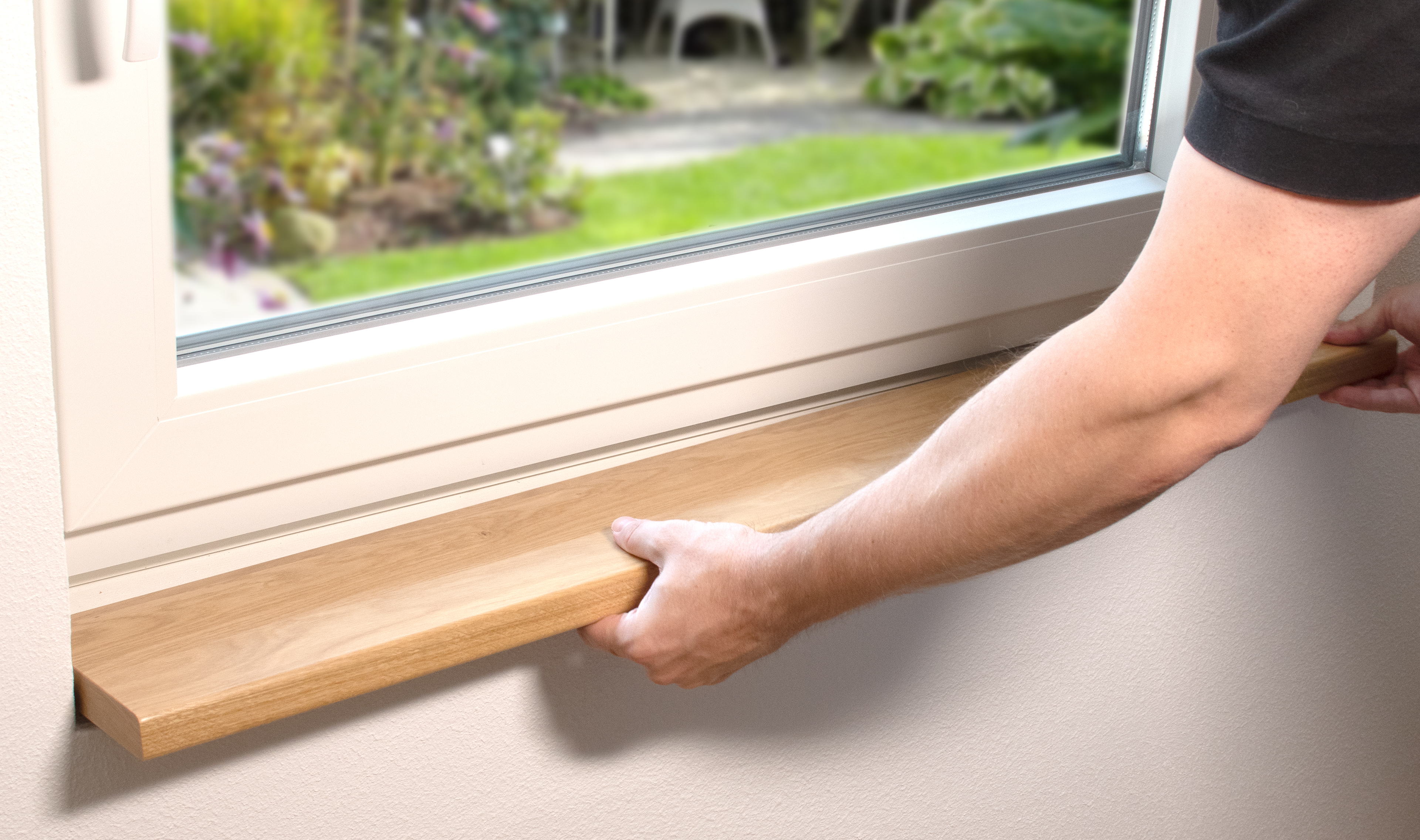 Alféizar de madera maciza en montaje: una mano coloca un alféizar claro bajo una ventana blanca, vista al jardín