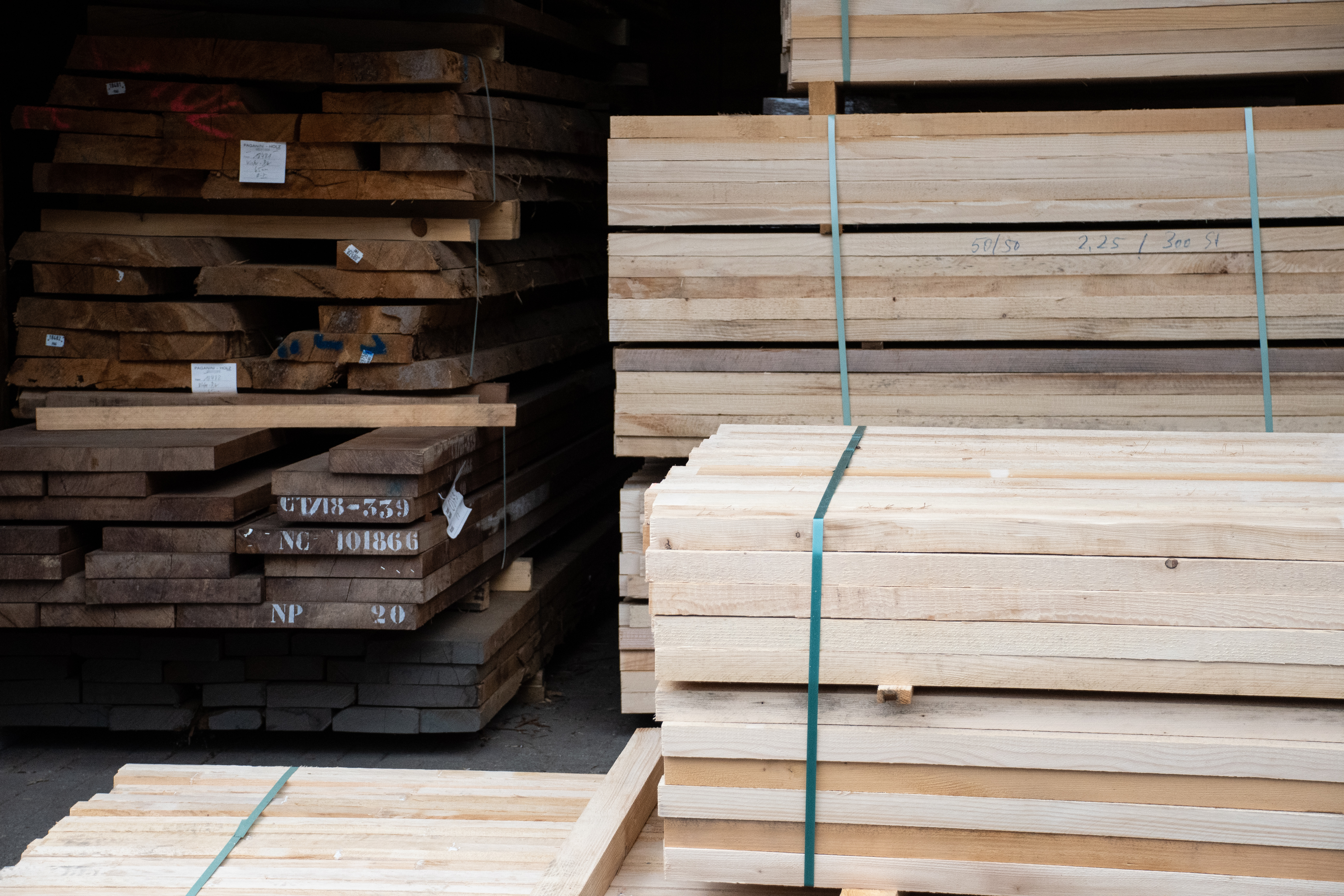 Almacén de madera con tablones macizos apilados y tablas claras en haces, materia prima para pasamanos de madera