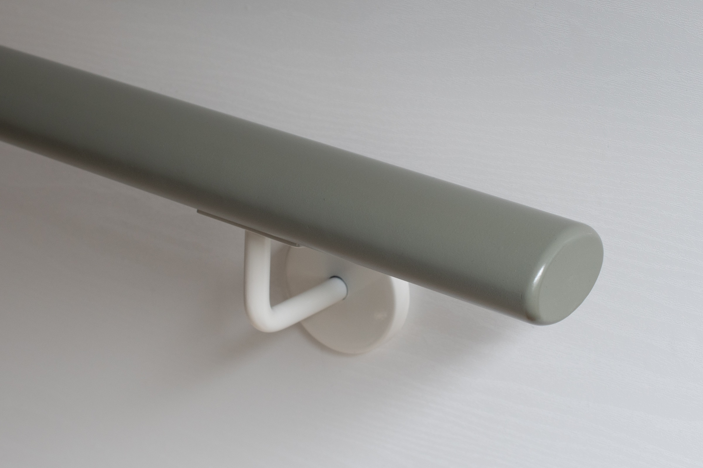 Pasamanos ovalado lacado gris con soporte de pared lacado blanco en pared clara, extremo con cantos redondeados